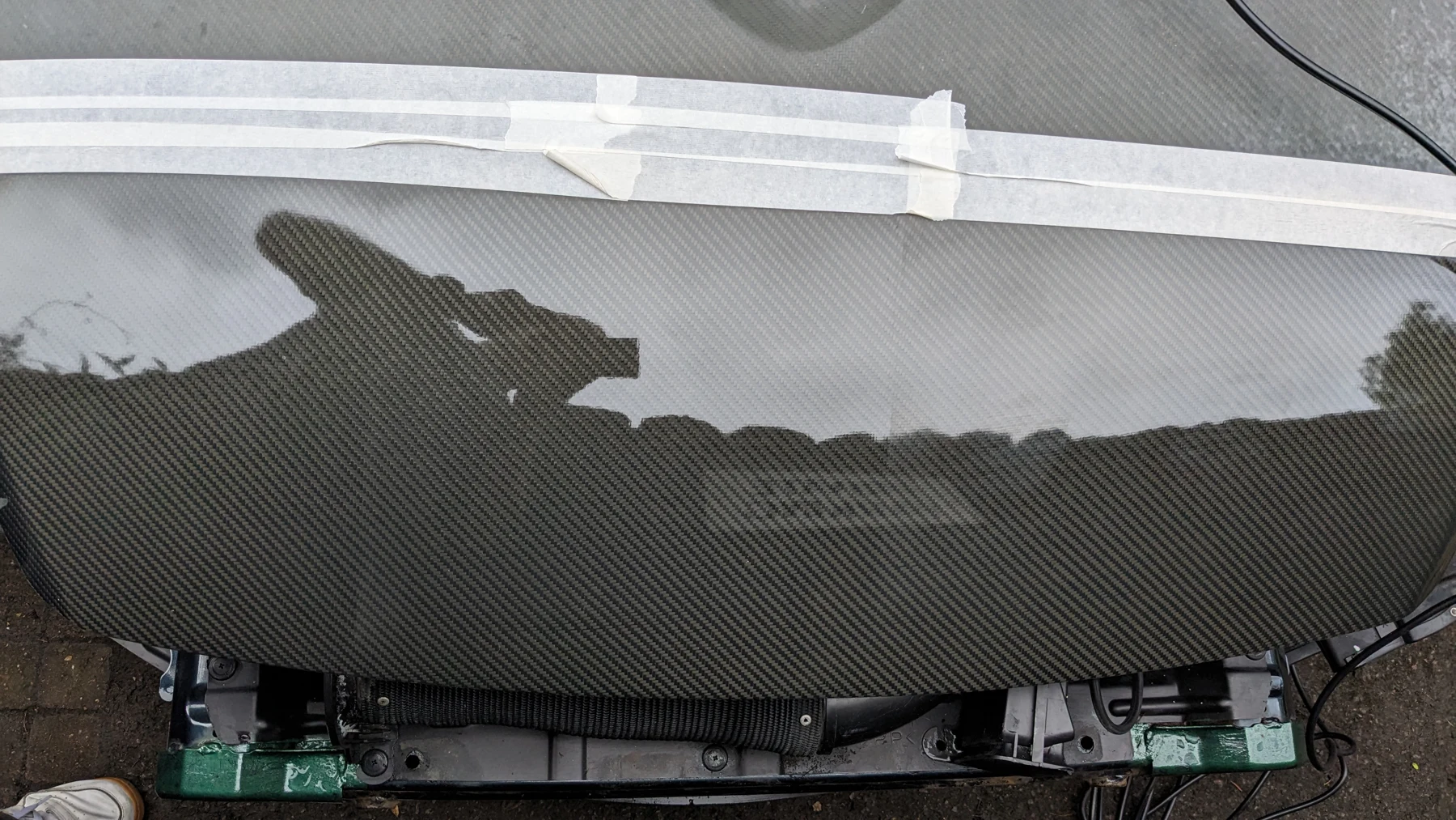Clear carbon weave and reflected surroundings on the restored bonnet, with masking tape still visible